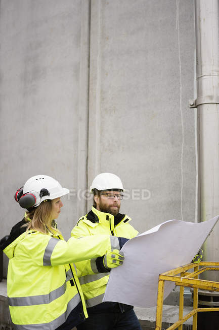 Man and woman in reflective clothing discussing blueprints — Stock Photo