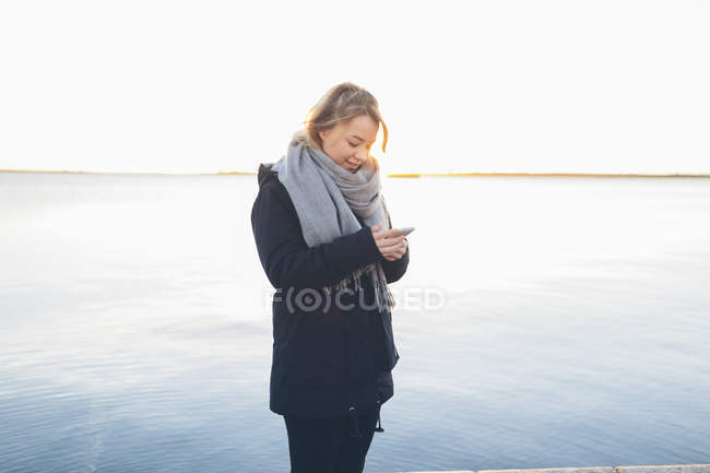 Frau nutzt Smartphone auf See — Stockfoto