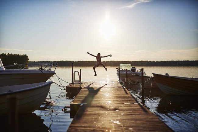 Вид ззаду хлопчика, що стрибає на пірсі на заході сонця — стокове фото