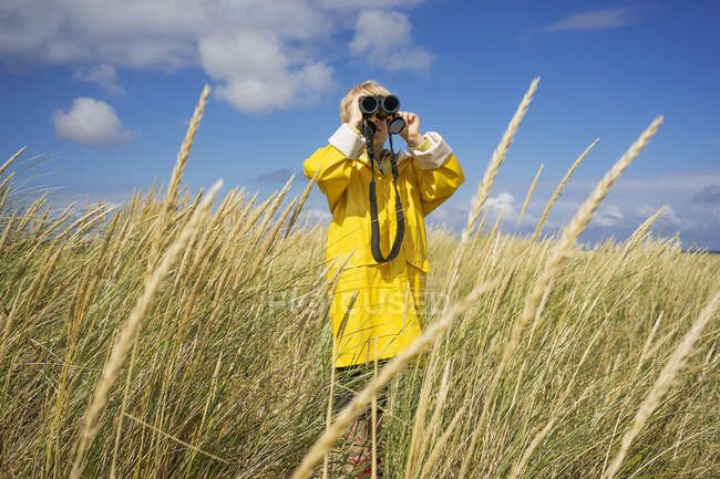 Boy in wet weather gear looking through binoculars — Stock Photo