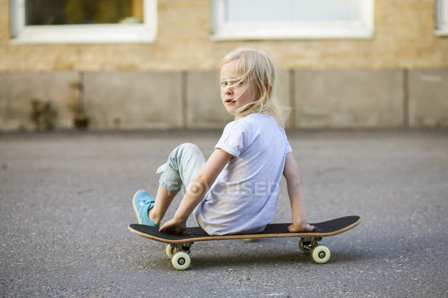 Girl sitting on skateboard, focus on foreground — Stock Photo