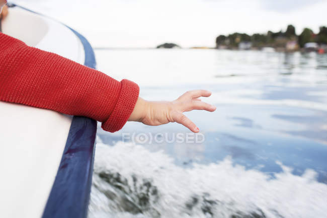 Обрізаний вид на дитину, що тягнеться до води з човна — стокове фото