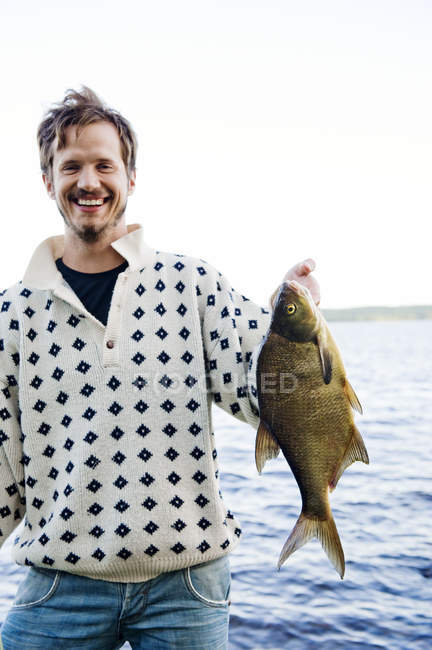 Улыбающийся человек держит пойманную рыбу у озера — стоковое фото