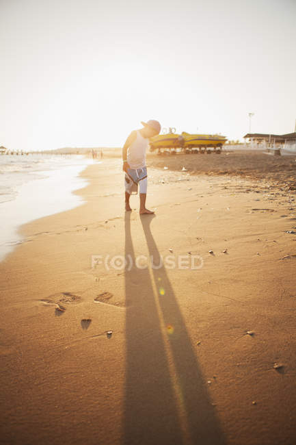 Garçon en vêtements décontractés marchant sur la plage au coucher du soleil — Photo de stock