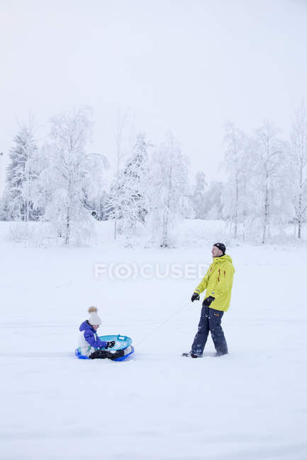 Вид сбоку отца, тащившего девочку на санках зимой — стоковое фото