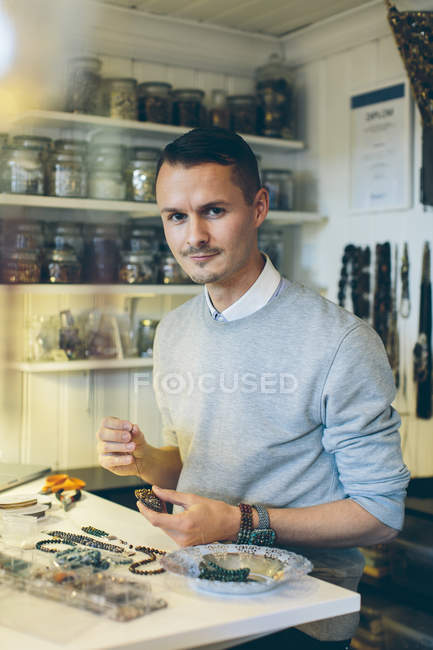 Man making beaded jewelry and looking at camera — Stock Photo