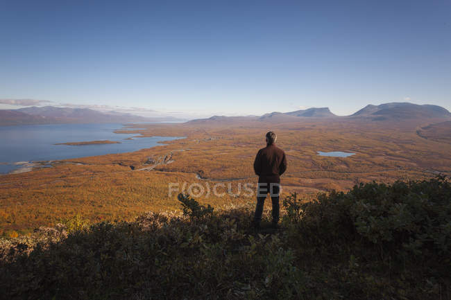 Rear view of man looking out across countryside to sea — Stock Photo