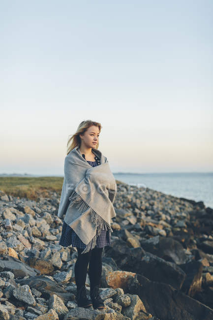 Young woman wrapped in shawl looking out to sea — Stock Photo