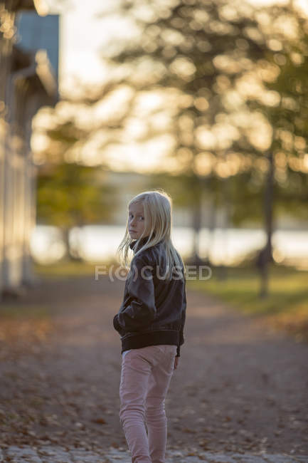 Retrato de niña caminando en el parque junto al río, mirando por encima del hombro - foto de stock