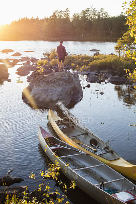 Uomo in piedi vicino a kayak su roccia al tramonto — Foto stock