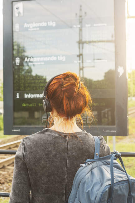 Rear view of woman in headphones by train sign — Stock Photo