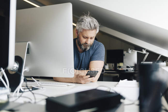 Businessman using smart phone at office desk — Stock Photo