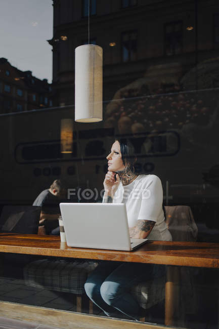 Femme utilisant un ordinateur portable, vue par la fenêtre — Photo de stock