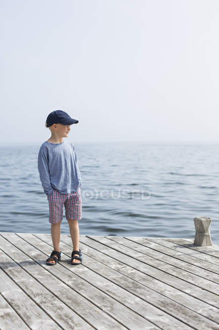 Menino de pé no molhe com as mãos nos bolsos — Fotografia de Stock