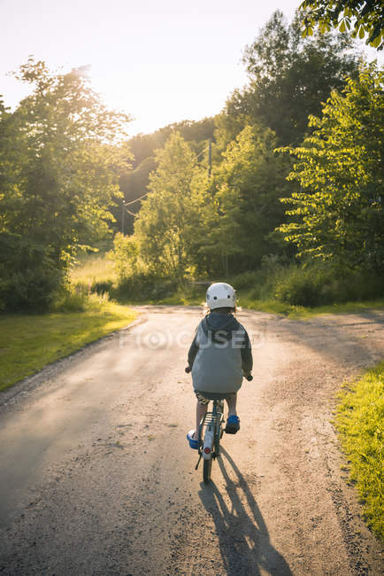 Вид сзади на мальчика, катающегося на велосипеде по асфальтированной дороге — стоковое фото