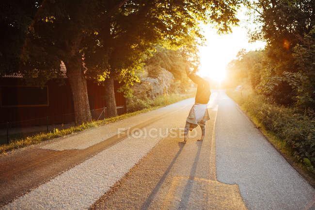 Homme faisant handstand sur la route au coucher du soleil — Photo de stock