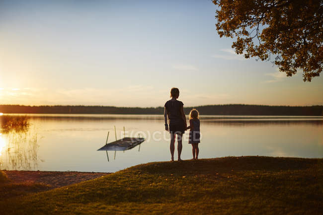 Вид ззаду матері і дочки на озері на заході сонця — стокове фото