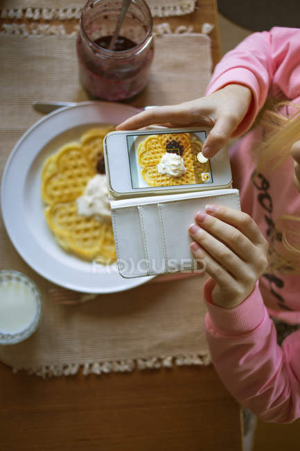 Девушка фотографирует бельгийские вафли на смартфоне — стоковое фото