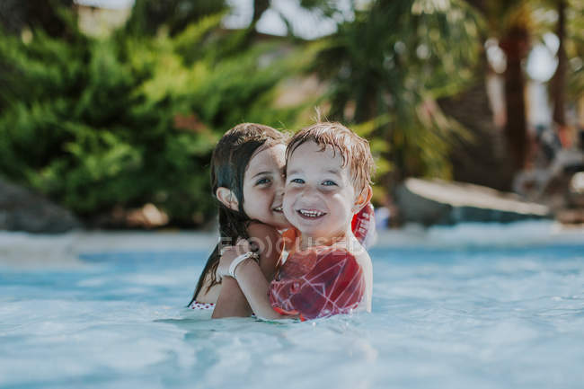 Deux jeunes enfants nagent dans la piscine et regardent la caméra — Photo de stock