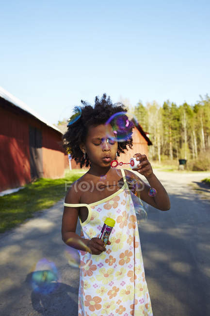 Chica soplando burbujas de jabón en el campo - foto de stock