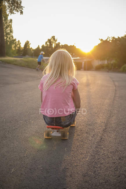 Rear view of girl sitting on red shortboard at street — Stock Photo