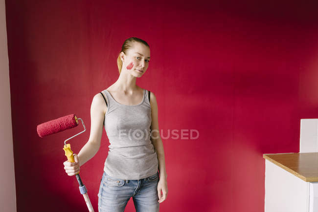 Portrait de femme avec rouleau de peinture contre mur rouge — Photo de stock