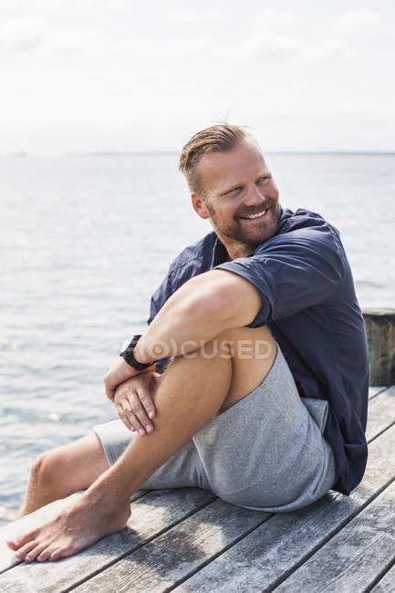Porträt eines Mannes, der auf einem Steg sitzt, Fokus auf Vordergrund — Stockfoto