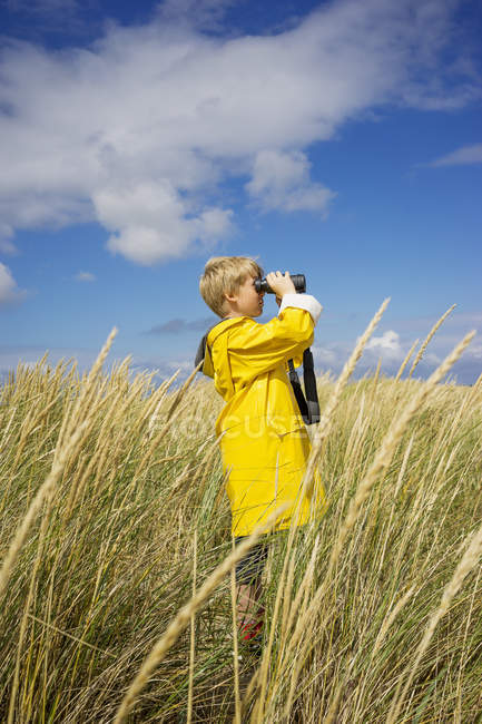 Rapaz com equipamento meteorológico molhado a olhar através de binóculos — Fotografia de Stock