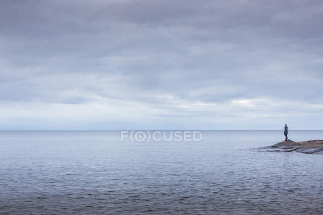 Mujer de pie sobre rocas por mar bajo cielo nublado - foto de stock