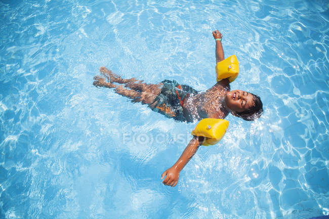Menino usando asas de água flutuando na piscina — Fotografia de Stock