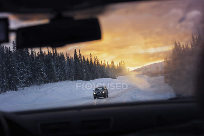 Auto durch Windschutzscheibe auf schneebedeckter Straße bei Sonnenuntergang gesehen — Stockfoto