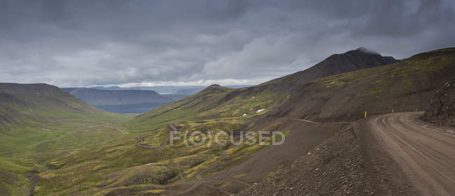 Camino de tierra en las montañas contra las nubes de tormenta, Islandia - foto de stock