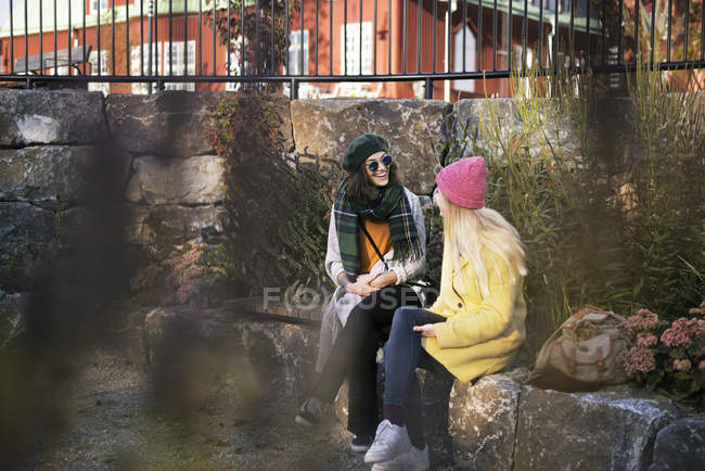 Dos mujeres jóvenes sentadas en la cornisa al aire libre, enfoque selectivo - foto de stock