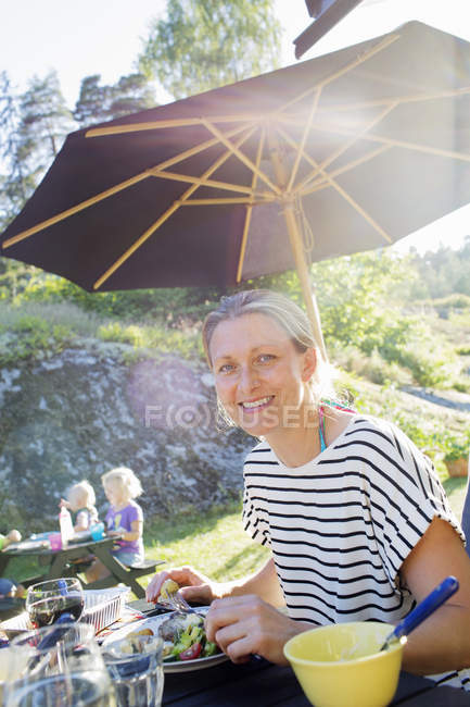 Усміхнена жінка їсть на відкритому повітрі, фокус на передньому плані — стокове фото