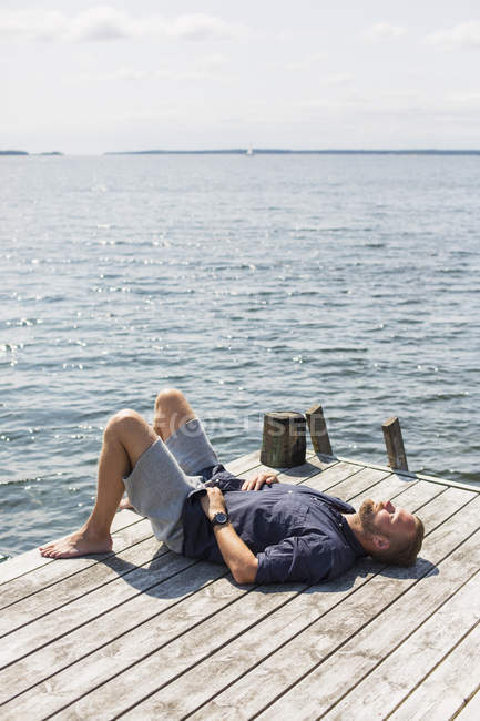Vista laterale di uomo prendere il sole sul molo vicino al mare — Foto stock