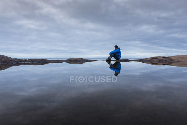 Чоловік сидить біля кам'яного басейну під похмурим небом — стокове фото