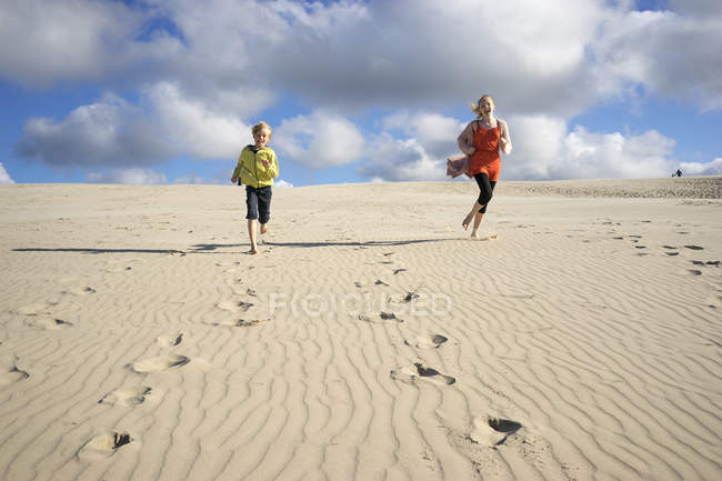Due bambini che corrono lungo la spiaggia sotto il cielo con le nuvole — Foto stock