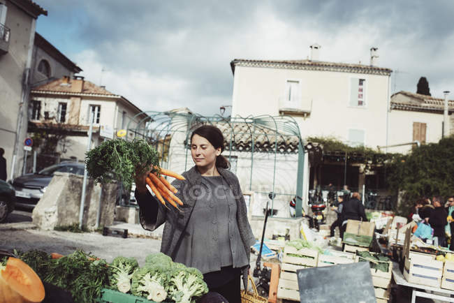 Mujer joven mirando zanahoria en el mercado - foto de stock