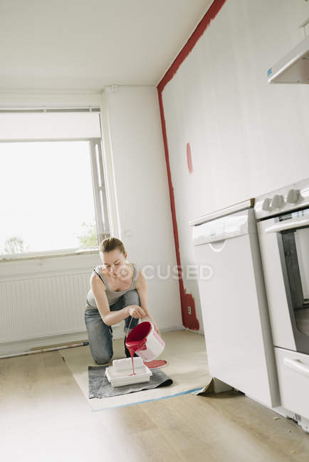 Mulher derramando tinta na bandeja de pintura na cozinha — Fotografia de Stock