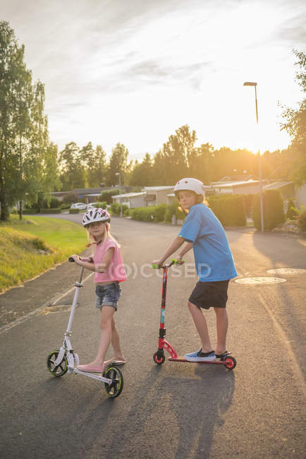 Portrait of girl and boy posing with push scooters in town street — Stock Photo
