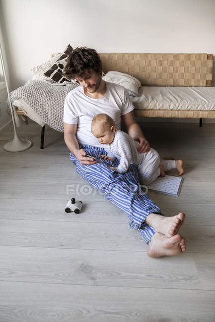 Pai e filho usando telefone inteligente na sala de estar — Fotografia de Stock