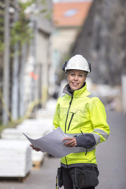 Obrero de la construcción sonriente con planos - foto de stock