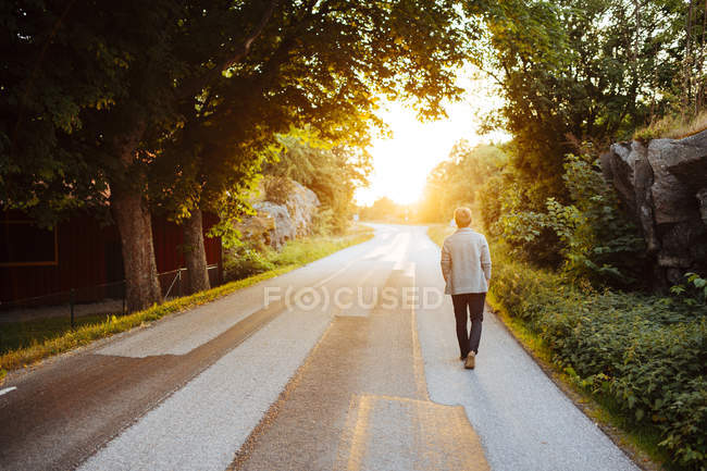 Vue arrière de l'homme marchant sur la route au coucher du soleil — Photo de stock