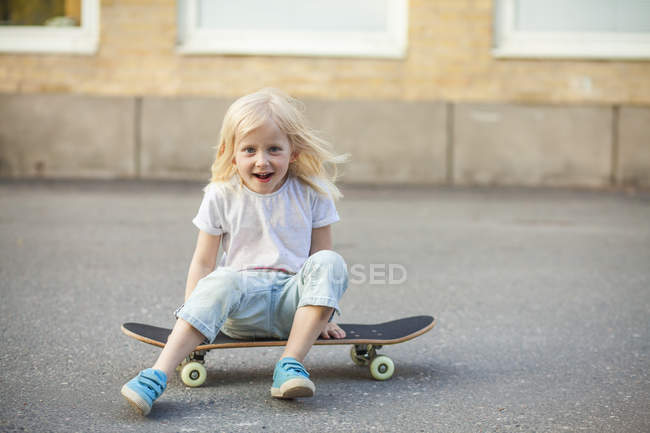 Девушка сидит на скейтборде, фокусируется на переднем плане — стоковое фото