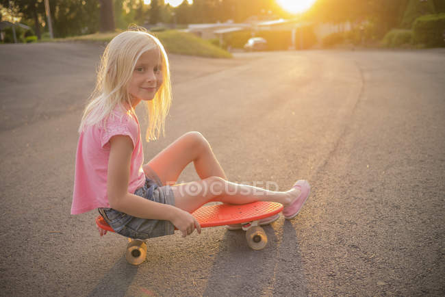 Portrait of girl sitting on red shortboard in street — Stock Photo