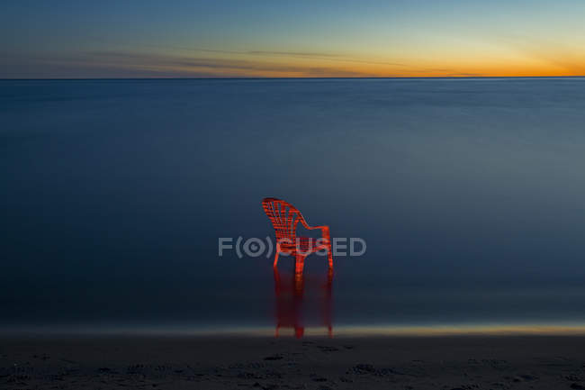 Красный стул на морском пляже на закате, фокусируйтесь на переднем плане — стоковое фото