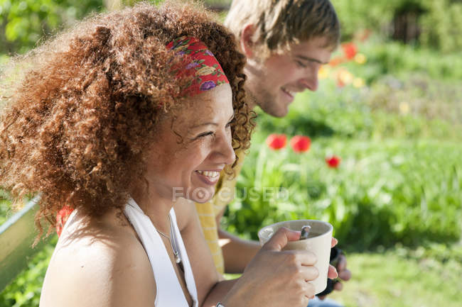 Молодая женщина и мужчина сидят на солнце и держа чашки — стоковое фото