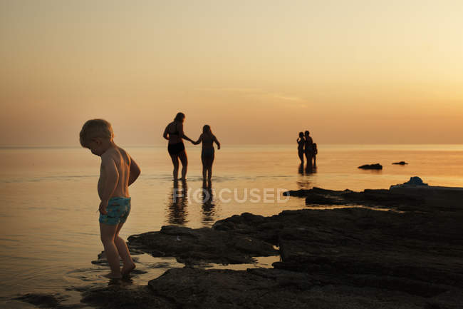 Niño con familia en la playa al atardecer, enfoque selectivo - foto de stock
