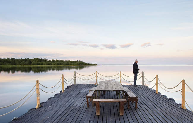 Uomo in piedi sul ponte di legno e guardando il mare — Foto stock