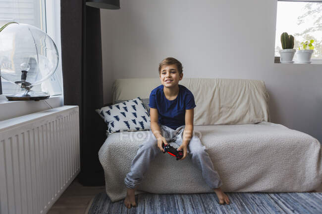 Boy on sofa with game console controller - foto de stock